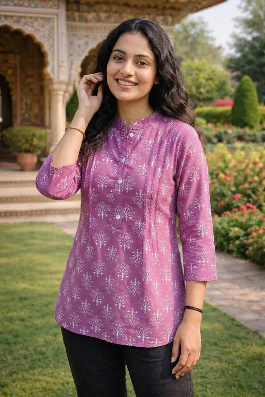 Woman wearing a purple patterned top outdoors with greenery in the background