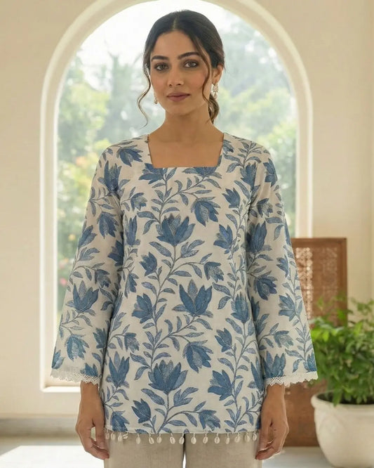 Woman wearing a blue floral patterned top in a bright room with a window in the background.