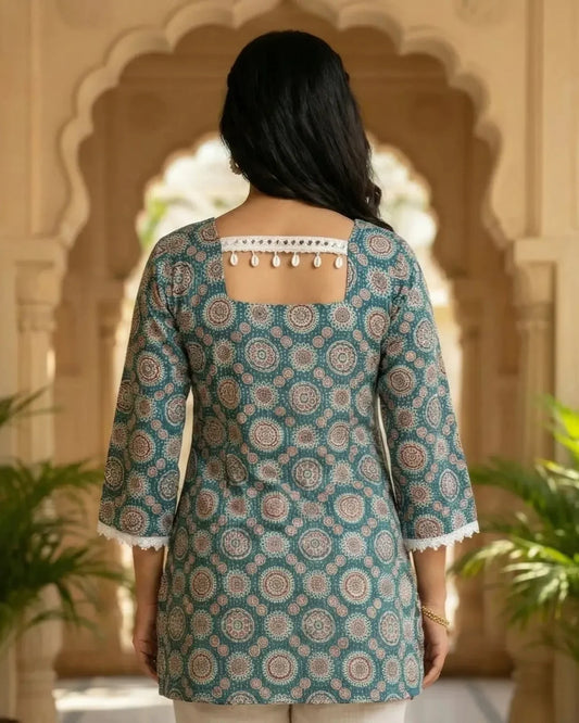 Woman wearing a patterned teal kurta with white trim in an outdoor setting.