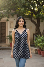 Woman wearing a black and white patterned top outdoors with greenery and a building in the background