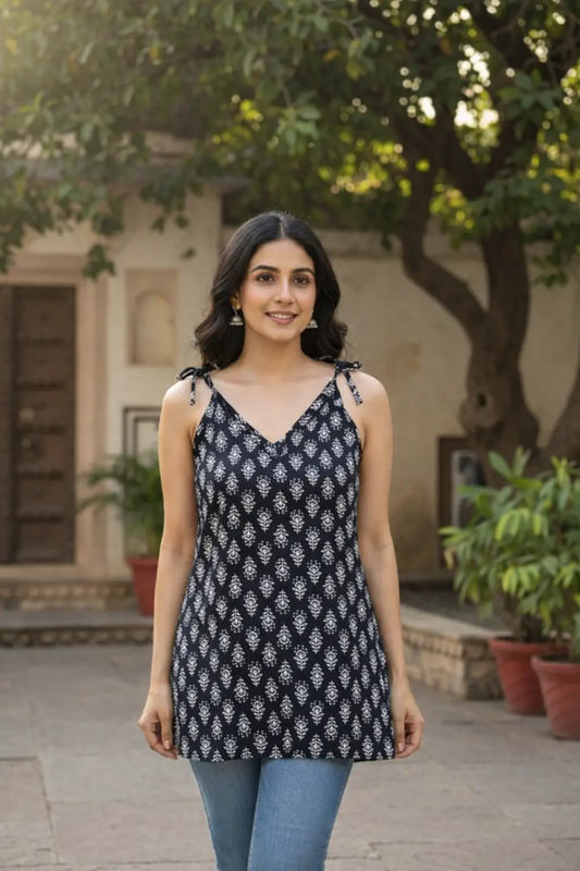 Woman wearing a black and white patterned top outdoors with greenery and a building in the background